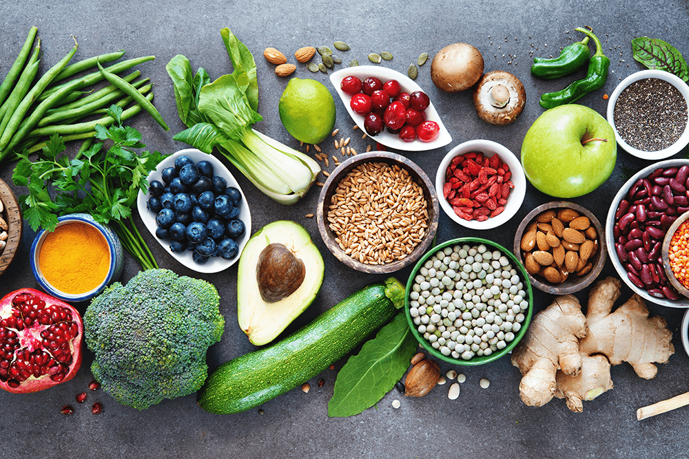 De nombreux aliments sains et bons pour la santé posés sur une table grise : fruits, légumes, graines...